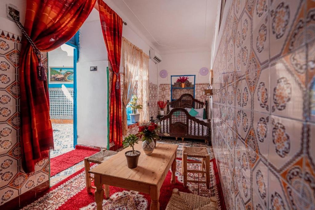 Chambre du riad avec fenêtre en arc ouverte sur les montagnes de l'Atlas, murs en tadelakt et lampe en laiton